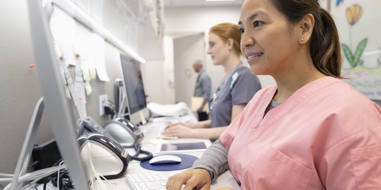 Woman in scrubs looking at computer monitor